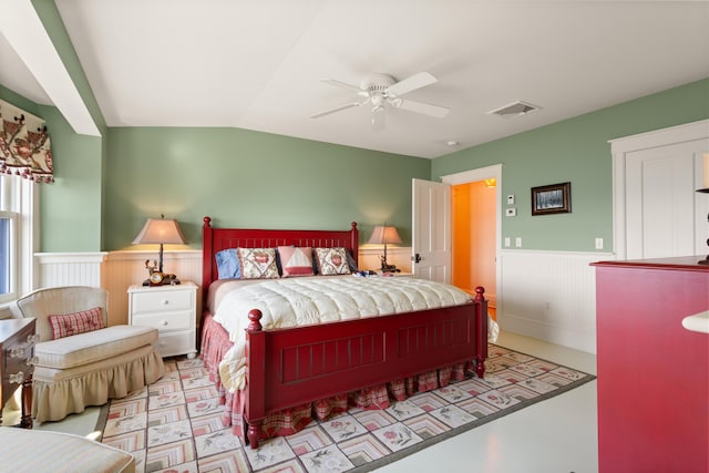 bedroom featuring ceiling fan, lofted ceiling, a wainscoted wall, and visible vents