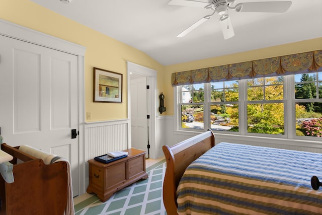 bedroom featuring lofted ceiling, a wainscoted wall, a ceiling fan, and multiple windows