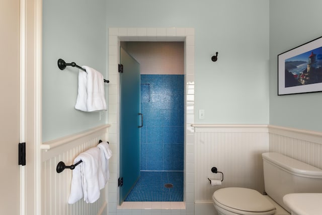full bathroom with a shower stall, a wainscoted wall, and toilet