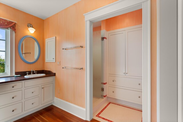 bathroom with baseboards, wood finished floors, vanity, and a shower