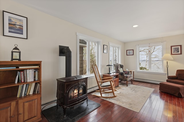 living area featuring a baseboard heating unit, plenty of natural light, a wood stove, and dark wood-type flooring