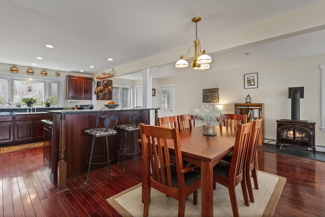 dining room featuring baseboard heating, recessed lighting, a wood stove, dark wood-style floors, and ornate columns