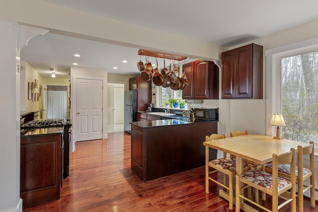 kitchen with dark wood-style floors, dark countertops, a sink, black appliances, and a peninsula