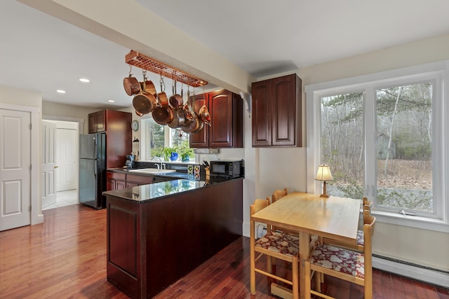 kitchen featuring a peninsula, a sink, dark countertops, dark wood-type flooring, and black appliances
