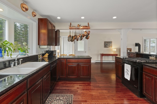 kitchen featuring a baseboard radiator, dark brown cabinets, a sink, black appliances, and dark wood-style flooring