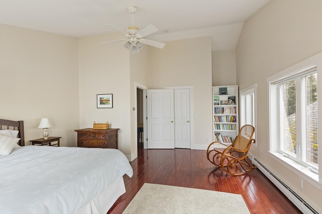 bedroom with a baseboard radiator, hardwood / wood-style floors, high vaulted ceiling, and multiple windows
