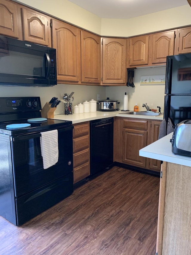 kitchen featuring dark wood-style floors, black appliances, a sink, and light countertops