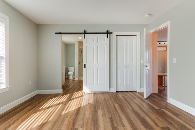 56 Old Kings Hwy, Ogunquit, ME 03907 - unfurnished bedroom featuring a closet, a barn door, wood finished floors, an AC wall unit, and baseboards