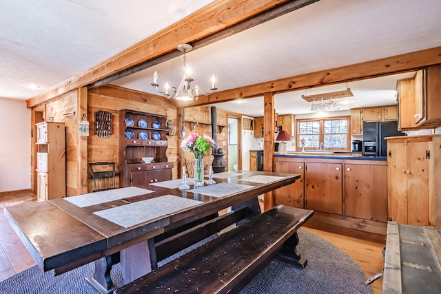 dining area with wood walls, beamed ceiling, light wood finished floors, and a notable chandelier