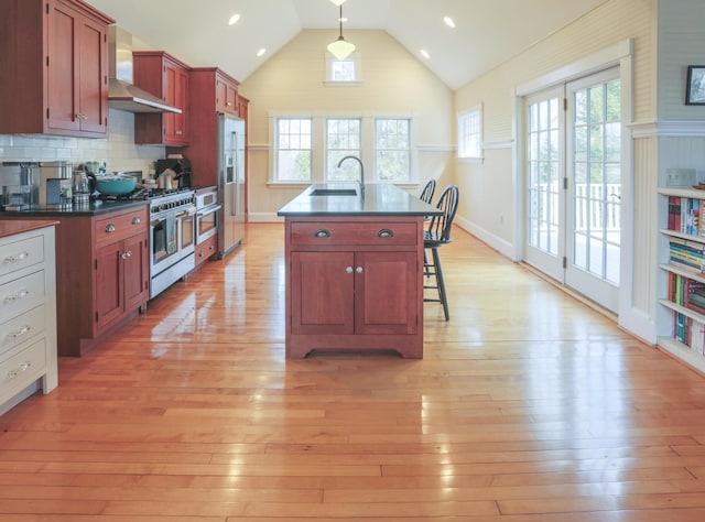 kitchen with premium appliances, dark countertops, a sink, and wall chimney range hood