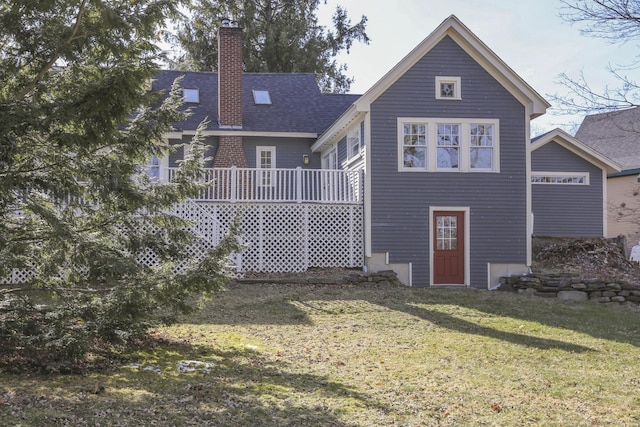 back of property featuring roof with shingles, a yard, a wooden deck, and a chimney