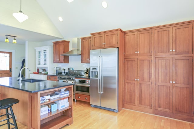 kitchen with dark countertops, wall chimney exhaust hood, brown cabinetry, appliances with stainless steel finishes, and a sink