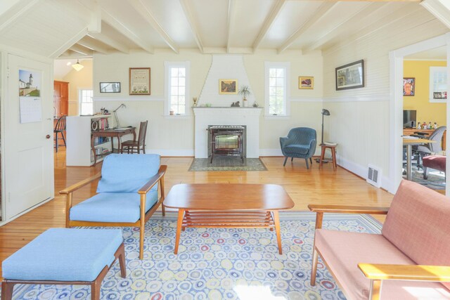 living area with baseboards, a wainscoted wall, visible vents, beamed ceiling, and wood finished floors
