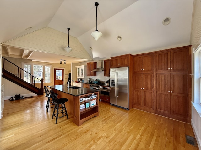 kitchen featuring light wood-style flooring, wall chimney range hood, a sink, dark countertops, and high end fridge
