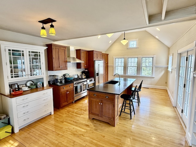 kitchen featuring wall chimney range hood, dark countertops, a breakfast bar area, appliances with stainless steel finishes, and a sink