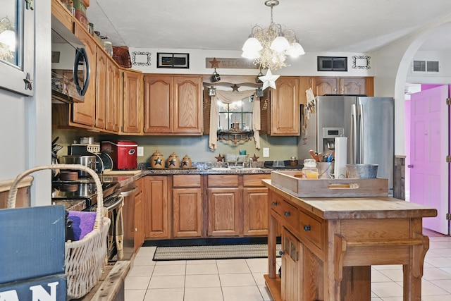 kitchen featuring black microwave, light tile patterned floors, arched walkways, stainless steel refrigerator with ice dispenser, and visible vents