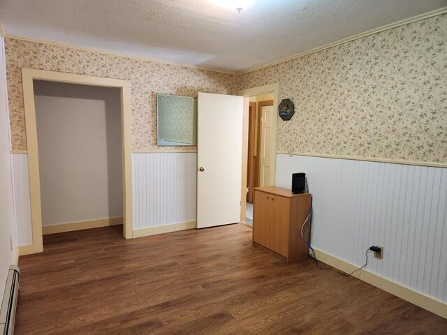 empty room with wainscoting, wallpapered walls, and wood finished floors