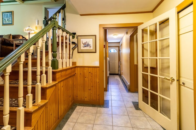 hallway with light tile patterned floors, ornamental molding, wainscoting, stairs, and wooden walls