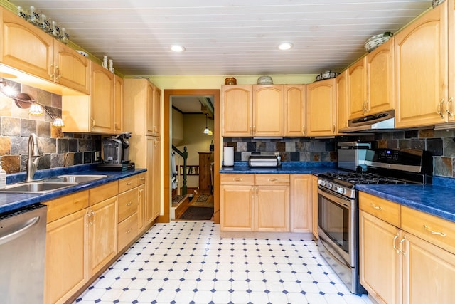 kitchen with under cabinet range hood, dark countertops, a sink, stainless steel appliances, and decorative backsplash