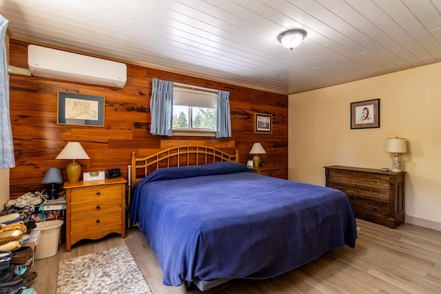 bedroom featuring wooden walls, an AC wall unit, baseboards, and wood finished floors