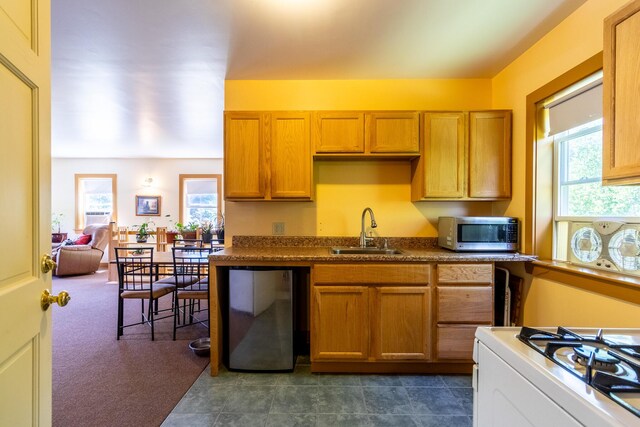 kitchen featuring stainless steel microwave, refrigerator, dark countertops, white gas range, and a sink