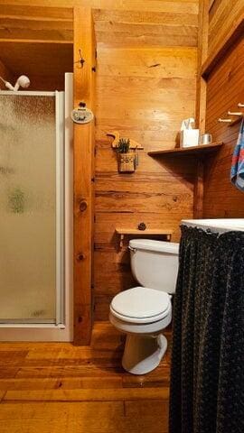 full bathroom featuring toilet, hardwood / wood-style flooring, wood walls, and a stall shower