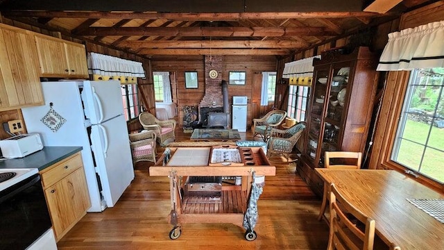 kitchen featuring electric stove, beamed ceiling, wood finished floors, light brown cabinets, and a wood stove