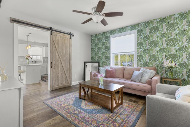 living room featuring wallpapered walls, an accent wall, ceiling fan, and a barn door