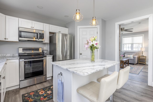 kitchen featuring light stone counters, a ceiling fan, wood finished floors, stainless steel appliances, and white cabinetry