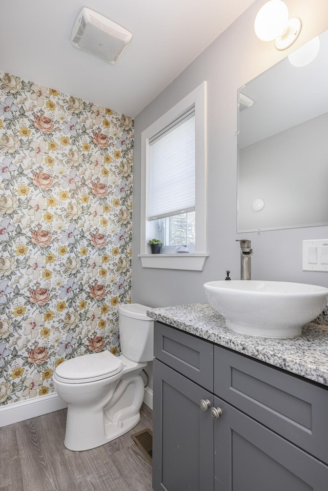 bathroom featuring toilet, baseboards, wallpapered walls, wood finished floors, and vanity