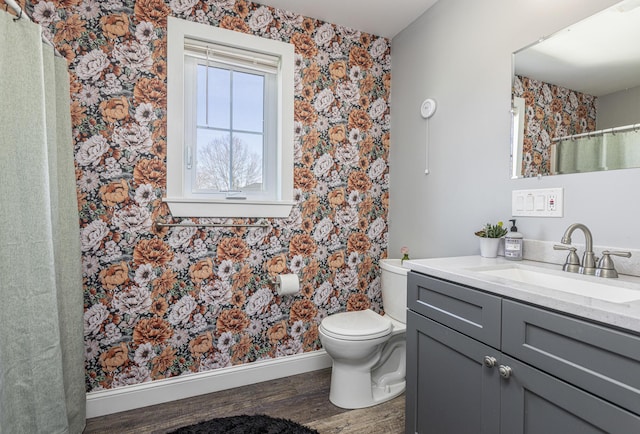 full bath with toilet, wood finished floors, wallpapered walls, vanity, and baseboards