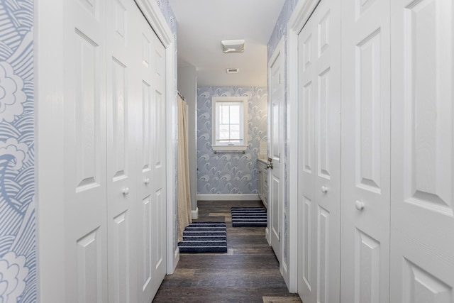 corridor featuring dark wood finished floors, wallpapered walls, visible vents, and baseboards