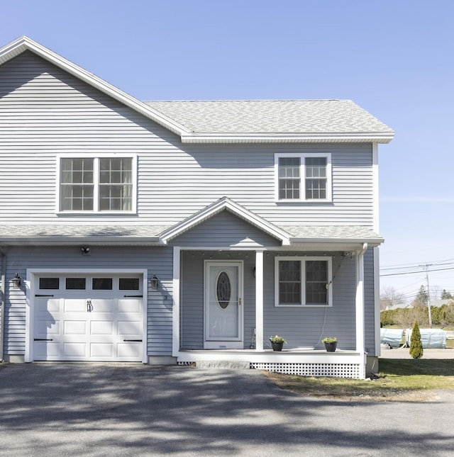 traditional-style home featuring a garage, a shingled roof, covered porch, and aphalt driveway