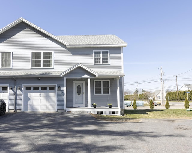 traditional-style house featuring an attached garage, aphalt driveway, roof with shingles, and covered porch