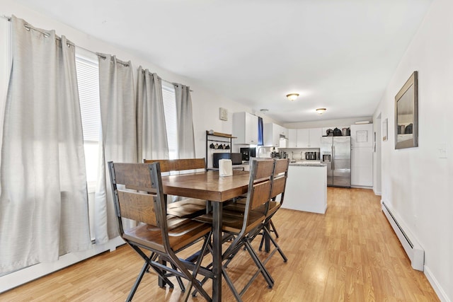 dining space featuring baseboard heating, light wood-type flooring, and baseboards