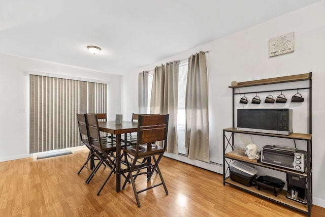 dining area with a baseboard radiator, wood finished floors, and baseboards