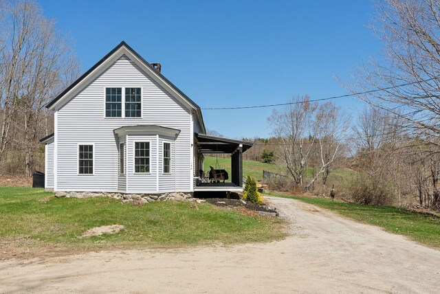 view of home's exterior with a porch, dirt driveway, a yard, and a chimney