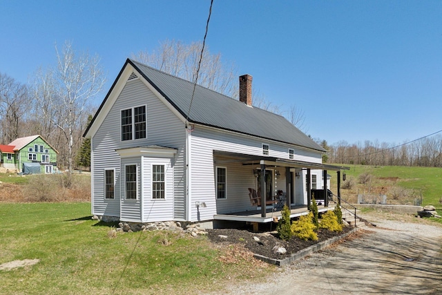 exterior space featuring a lawn, covered porch, a chimney, and metal roof