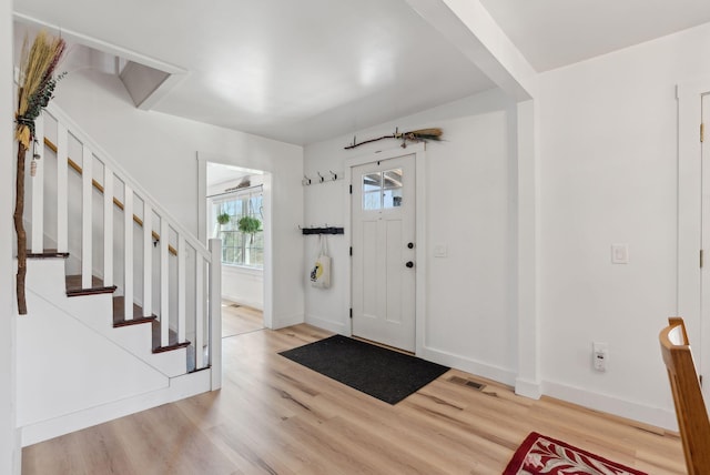 foyer entrance with stairway, baseboards, and light wood finished floors