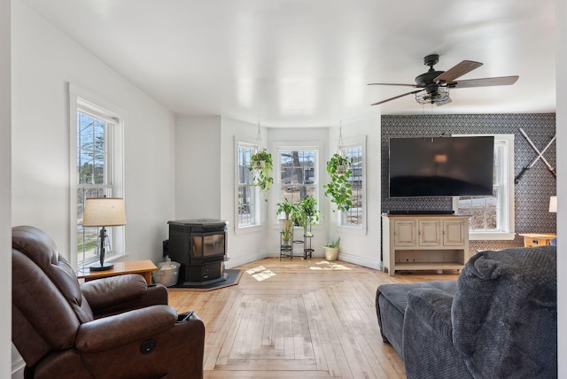 living area featuring a ceiling fan, a wood stove, hardwood / wood-style flooring, and a wealth of natural light