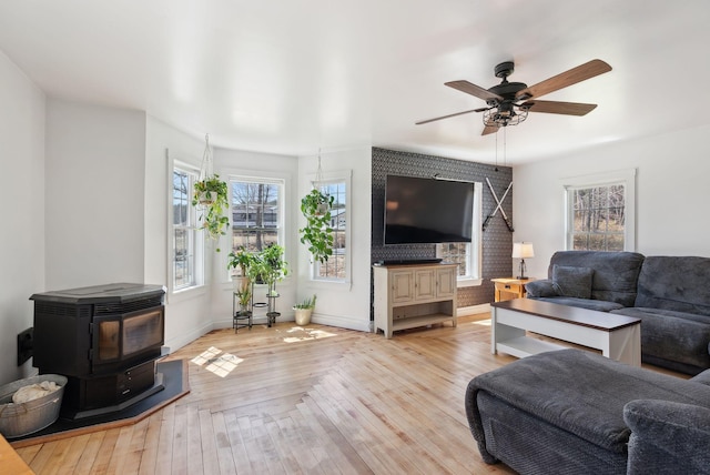 living room featuring a ceiling fan, a wealth of natural light, a wood stove, and wood finished floors