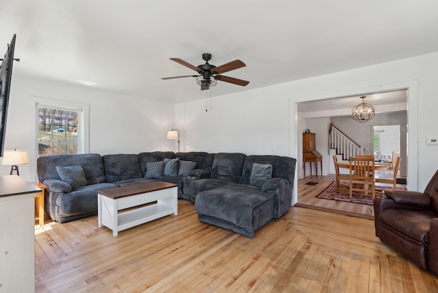 living room with light wood-type flooring, ceiling fan with notable chandelier, a wealth of natural light, and stairway