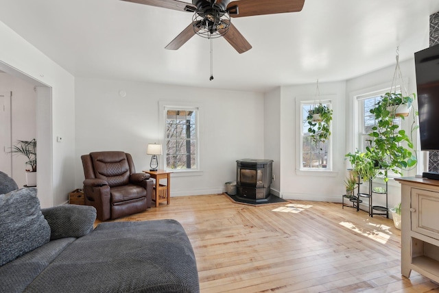 living room featuring baseboards, ceiling fan, a healthy amount of sunlight, and a wood stove