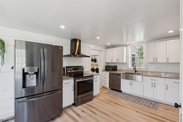 kitchen with a sink, light wood-style flooring, wall chimney exhaust hood, stainless steel appliances, and white cabinetry
