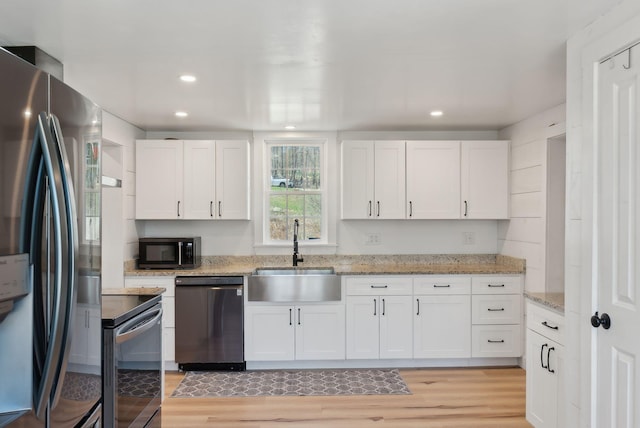 kitchen featuring white cabinets, a sink, light wood finished floors, stainless steel appliances, and recessed lighting