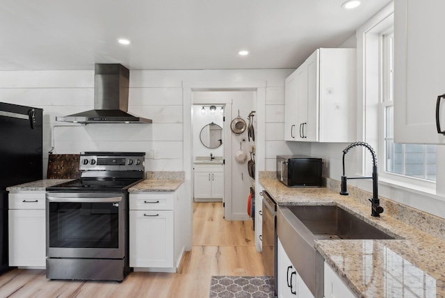 kitchen with wall chimney range hood, a sink, electric stove, white cabinetry, and light wood-type flooring