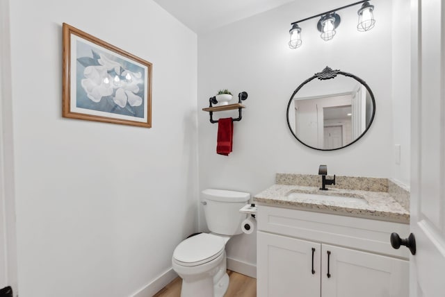 half bath featuring baseboards, wood finished floors, toilet, and vanity