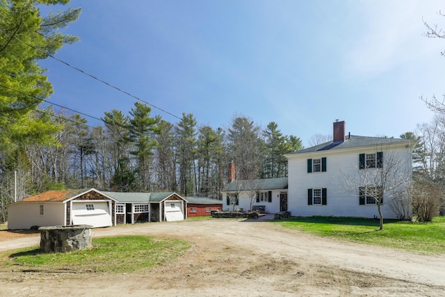 view of front of home featuring a chimney, an outdoor structure, dirt driveway, and an attached garage