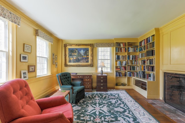 living area featuring a fireplace with flush hearth, baseboards, built in shelves, wood finished floors, and crown molding