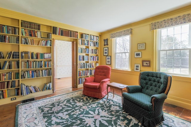 sitting room with built in shelves, ornamental molding, a wealth of natural light, and wall of books